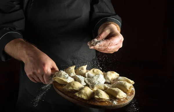 Stock image Professional chef throws flour to raw dumplings on a cutting kitchen board before cooking. Black space for menu or recipe