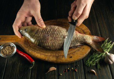 Ahşap bir mutfaktaki sazan balığını bıçakla aşçının elleriyle kesmek. Restoran mutfağında balık diyeti yapmak.