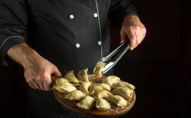 Aşçı çiğ hamur köftesini bir mutfak aletiyle alır ve çevirir. Mutfaktaki hamur köfteleri şefin elindeki kesim tahtasının üzerinde. Menü veya tarif için siyah boşluk