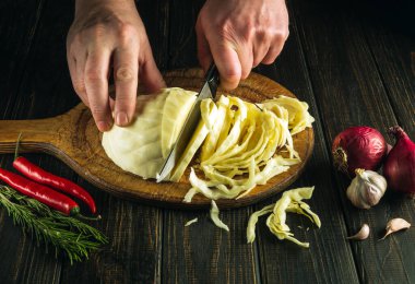 Aşçının elleri bıçakla taze lahana kesiyor. Antika mutfak masasında salata için taze sebzelerle birlikte. Aşçılık ve restoran konsepti