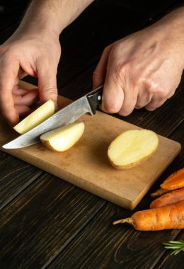 Aşçı ahşap bir kesme tahtasıyla taze patates keser. Sebzeli vejetaryen yemeği hazırlarken şefin ellerini yakın plan çek.