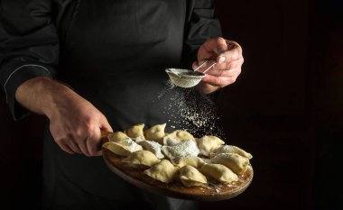 Profesyonel şef pişirmeden önce kesme tahtasındaki çiğ hamur köftelerine pudra şekeri ekler. Menü veya tarif için siyah boşluk