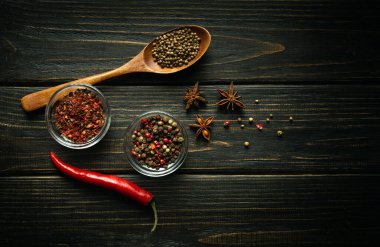Siyah bir masada kırmızı biber ve çeşitli baharatlar. Cam bardaklarda ve kaşıkta baharatlar. Tarif veya menü için karanlık boşluk.