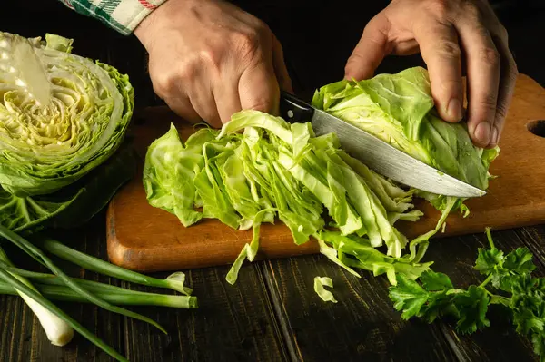 stock image Slicing cabbage on a cutting board. Delicious salad for dinner with fresh vegetables. Hands of a chef with a knife while cooking in a kitchen.