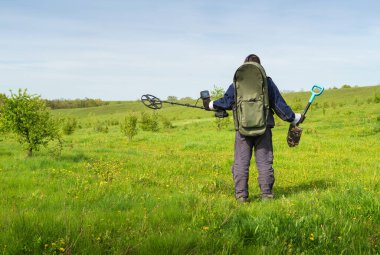 Metal detektörlü bir adam. Metal detektörü ve kameraya arkası dönük küreği olan adam. Hazine Avcısı arama işini yürütür. Kazıcı metal aramak için dedektör kullanır.