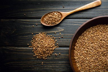 Pişirmeden önce eski bir masada kaşığın yanında bir tabak karabuğday homurtusu ve şekerleme. Siyah arkaplanda tarif veya menü için yer