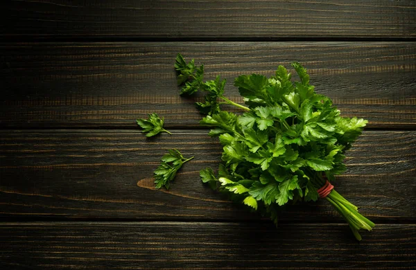 Lezzet ve koku için yiyeceğe eklenmeden önce karanlık bir mutfak masasında taze kokulu maydanoz. Menü veya tarif için boşluk.