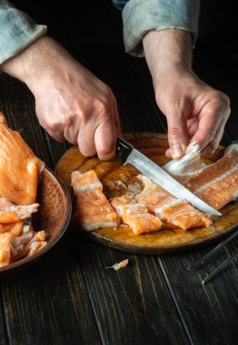 Tuzlamadan önce mutfak tahtasındaki kırmızı balıkları kesmek. Alabalık temizlerken bıçaklı bir aşçının elleri. Balık diyeti fikri..