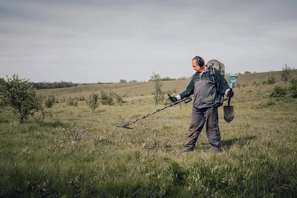 A man with a metal detector with his back to the camera. Man in sportswear with a metal detector. Digger on a summer meadow. The concept of searching for coins underground. Digger with metal detector.