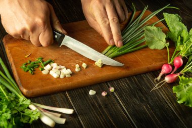 Bıçaklı bir aşçının elleri vejetaryen yemeği pişirmek için kesme tahtasına soğan kesiyor. Mutfak masasındaki köylü ürünleri..