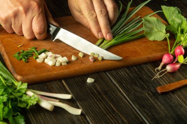 Vejetaryen yemeği hazırlamak için kesme tahtasına yeşil soğan kesen bir şefin yakın çekimi. Mutfak masasında vejetaryen salatası hazırlıyorum..