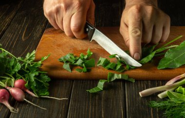 Restoranın mutfağında sebze tabakları pişiriyorum. Rumex 'i mutfak masasında bir şefin elinde bıçakla dilimlemek ya da tahta kesmek..