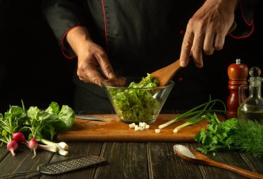 Şef bir kasede marul yaprakları karıştırır. Restoran mutfağında çalışma ortamı. Taze sebzeli leziz salata, aşçının elleriyle..