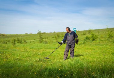 Metal dedektörlü bir adam çayırda hazine arıyor. Bir alet ve kürekle hazine avı.