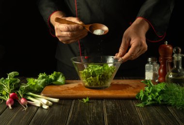 Profesyonel şef taze marul salatasına kaşıktan tuz ekler. Mutfakta vejetaryen yemeği pişirmek. Restoran veya otel menüsü.