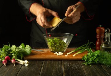 Şef mutfak masasındaki salata kasesine peynir ekler. Mutfakta aşçının elleriyle vejetaryen yemeği pişirmek.