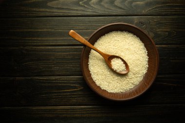 Yemek ya da yulaf lapası hazırlamadan önce bir tabak beyaz pirinç ve bir kaşık mahsul masasında. Koyu arkaplanda tarif veya menü için yer