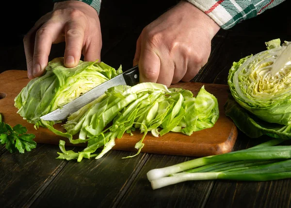 stock image The chef cuts fresh green cabbage on a cutting board with a knife. Close-up of a cook hands while working on a kitchen table. Vegetarian or vegetable diet idea