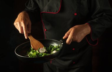 The chef prepares food in a frying pan with steam on a black background. The concept of restaurant and hotel service. Asian cuisine.