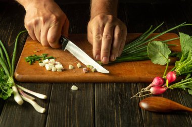 Şef restoranın mutfağında bir salata hazırlar. Aşçı ellerinin kesme tahtasındaki bir bıçakla taze soğan keserken yakın çekimi. Mutfak masasında taze vejetaryen yemeği..