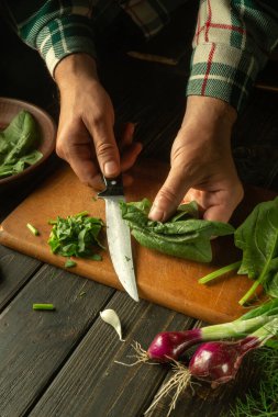 Kesme tahtasındaki bıçakla ıspanak dilimlemek. Mutfakta bir aşçının elinden sebze salatası pişirmek. Vejetaryen diyeti fikri.