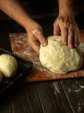 Erkek bir fırıncının elinin un tozuyla mutfak tahtasındaki hamuru yoğuruşunun yakın çekimi. Pişirme ve şekerleme konsepti.