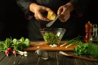 Restorandaki mutfak masasında vitamin salatası hazırlığı. Şefin elleri rende kullanarak salataya peynir ekliyor. Vejetaryen ürünleri.