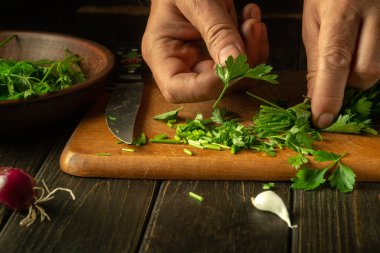 Aşçı mutfak masasında kokulu maydanozlu ve sebzeli bir salata hazırlıyor. Bir restoran ya da kafe için bir şefin elinden sebze salatası pişirme kavramı..