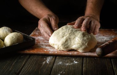 Erkek bir fırıncının elinin un tozuyla mutfak tahtasındaki hamuru yoğuruşunun yakın çekimi. Pişirme ve şekerleme konsepti
