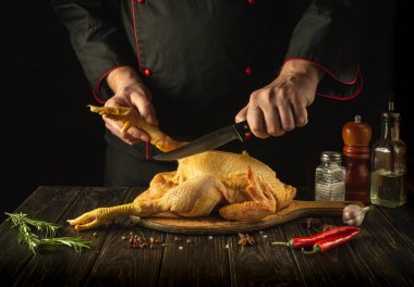 Slicing raw chicken with a knife in the hand of a cook in a restaurant kitchen. Getting ready to make crispy nuggets. Chicken dish concept on dark background