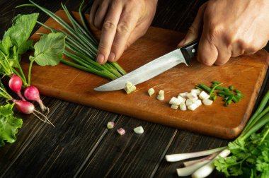Bıçaklı şef vejetaryen yemeği pişirmek için bir kesme tahtasına soğan kesiyor. Mutfak masasında köylü yemeği.