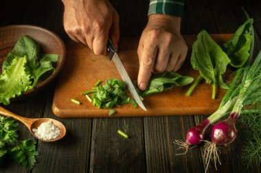 Aşçı mutfak tahtasındaki taze sebzeli salata için taze ıspanakla bıçak kesiyor. Restoran ya da kafe için sebze salatası pişirme kavramı..