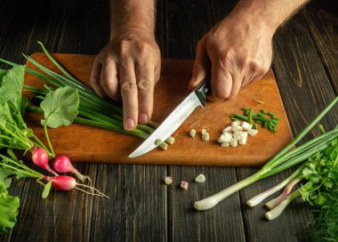 Şefin elleri, vejetaryen yemeği hazırlamak için mutfak tahtasındaki taze yeşil soğanları dilimliyor. Restoran mutfağında sebze diyeti fikri...