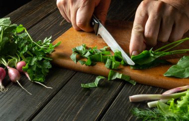 Şef restoran mutfağında ıspanak salatası hazırlıyor. Kesme tahtasındaki bıçakla sebze kesen bir aşçının yakın çekimi. Mutfak masasında taze vejetaryen yemeği..