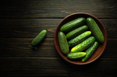 Koyu renk mutfak masasında salatalık turşusu için hazırlanmış antika bir tabakta taze yeşil salatalık. Salatalık topluyorum..