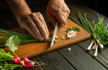 Şef, öğle yemeği için bir beslenme vitamini tabağı hazırlamak için taze yeşil soğanı kesme tahtasıyla keser..