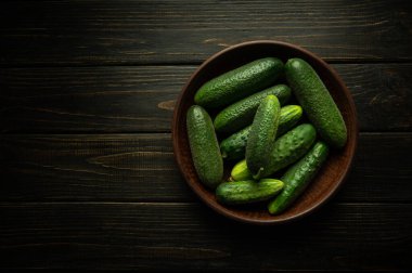 Antika bir tabakta taze yeşil salatalıklar ve vejetaryen yemeği için hazırlanmış koyu bir mutfak masasında. Boşluğu kopyala.