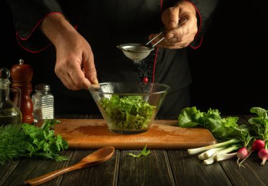 Profesyonel şef biberli marul yapraklarını kasede doğradı. Bir otel mutfağında çalışma ortamı. Taze sebzeli lezzetli salata.