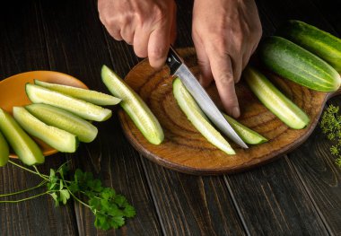 Öğle yemeğinde salatalık ve maydanozlu lezzetli bir salata. Mutfak tahtasının üzerinde salatalık doğrayan bıçaklı aşçı elleri..