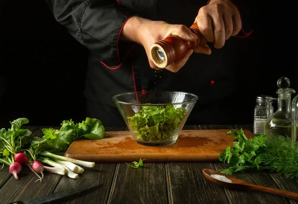 stock image Preparation of vitamin salad on the kitchen table in the restaurant. The chef adds pepper to the salad with his hands using a grinder. Vegetarian foods for the diet.