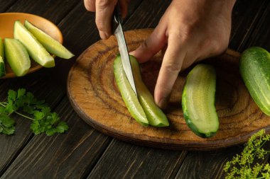 Aşçı salatalığı bir bıçakla turşu turşusu için uzunlamasına parçalara ayırır. Mutfak masasında salatalık ve maydanozlu çalışma ortamı..