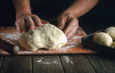 Fırıncı pastalar için un tozuyla mutfak tahtasındaki hamuru yoğurur. Fırında fırın ve hamur işi kavramı.