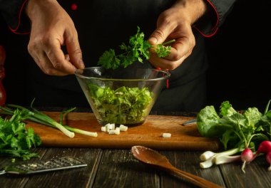 Profesyonel şef kasede taze sebze salatası hazırlıyor. Mutfak masasında çalışma ortamı. Taze sebzeli leziz salata, aşçının elleriyle.