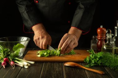 Şef restoran mutfağında bir salata hazırlıyor. Kesme tahtasındaki bıçakla sebze kesen bir aşçının yakın çekimi. Mutfak masasında taze vejetaryen yemeği..