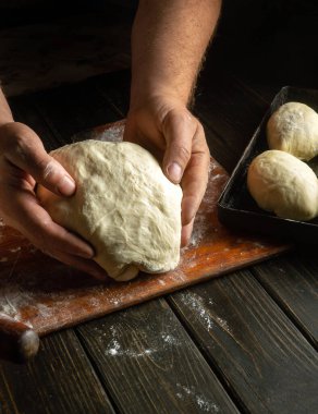 Fırıncının elleri hamur için mutfak masasının üzerindeki çörekleri yoğurur. Fırında turta pişirme konsepti.