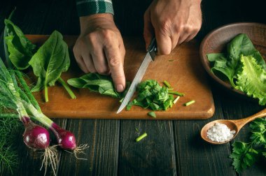 Şef, mutfak tahtasındaki taze sebzeli salata için taze ıspanakla bıçak kesiyor. Restoran için sebze salatası pişirme konsepti
