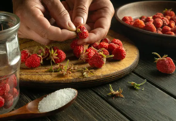 Close-up of the hands of the cook sorting strawberries on the kitchen table for making fruit drink in a jar.