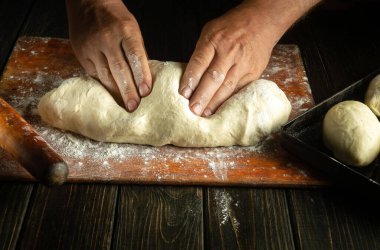 Çörekleri pişirmeden önce hamuru yoğuran aşçının ellerini yakın plan çek. Pastanedeki mutfak masasında çalışma ortamı.