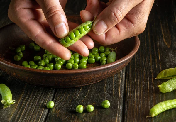 Close-up of male hands clean green pea pods. Work environment on the kitchen table. Cooking peas for breakfast or dinner.