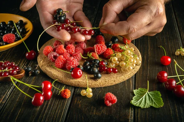 Close-up of male hands picking berries to make fruit drink or vitamin compote. The concept of a vegetarian drink made from currants, raspberries and cherries